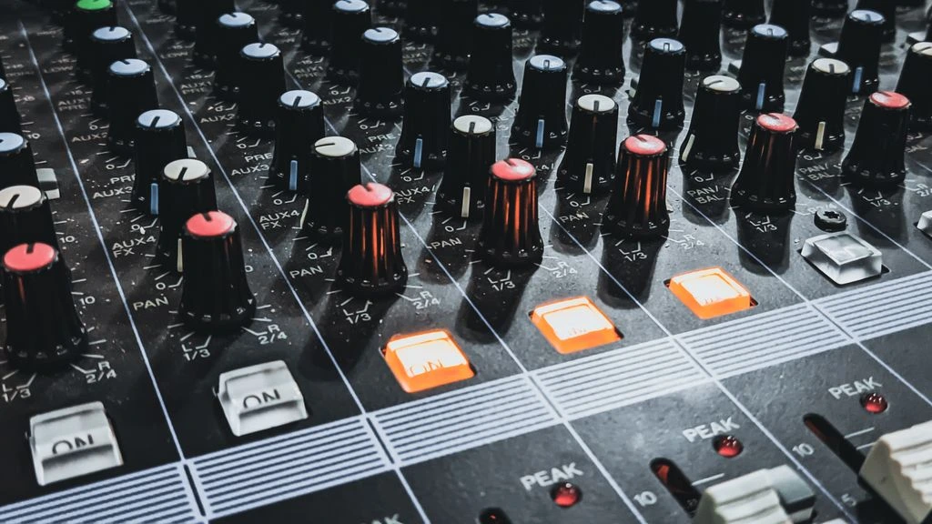 An analog mixing console lit by warm tungsten light inside a dim Brooklyn recording studio.